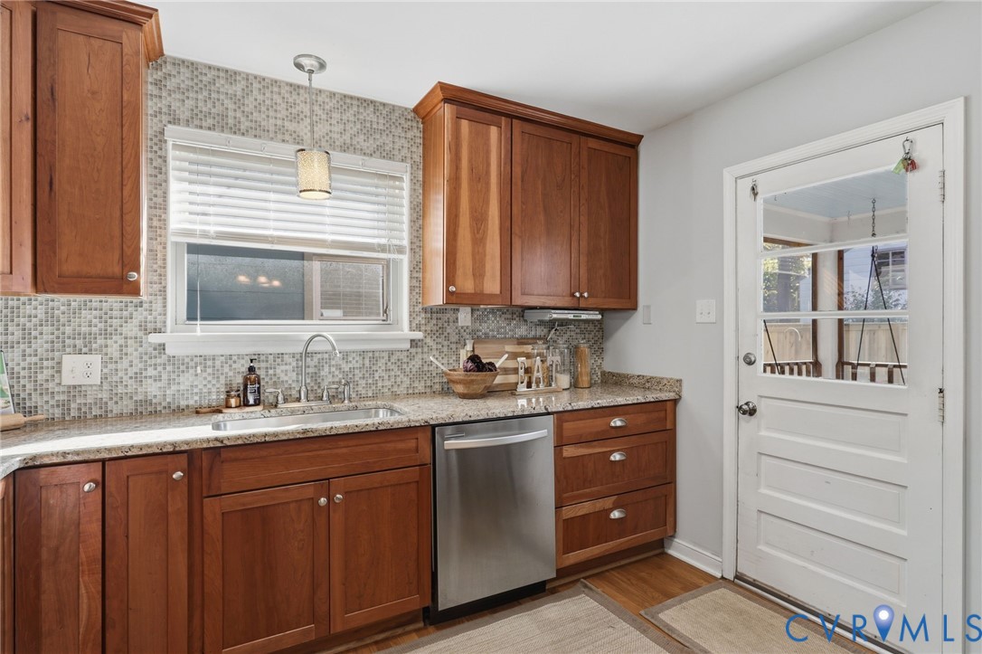 Kitchen featuring stained wood cabinetry, stone-finish countertops, mosaic tile backsplash, stainless steel dishwasher, and a glass-paneled exterior door