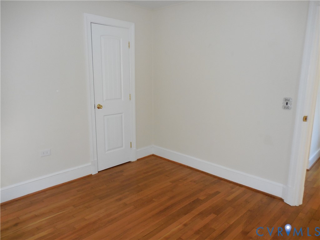 Interior room featuring wood-finish flooring, white walls, and a two-panel interior door with metallic hardware