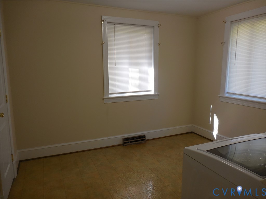 Interior space featuring neutral-toned walls, two windows with horizontal blinds, and tile flooring