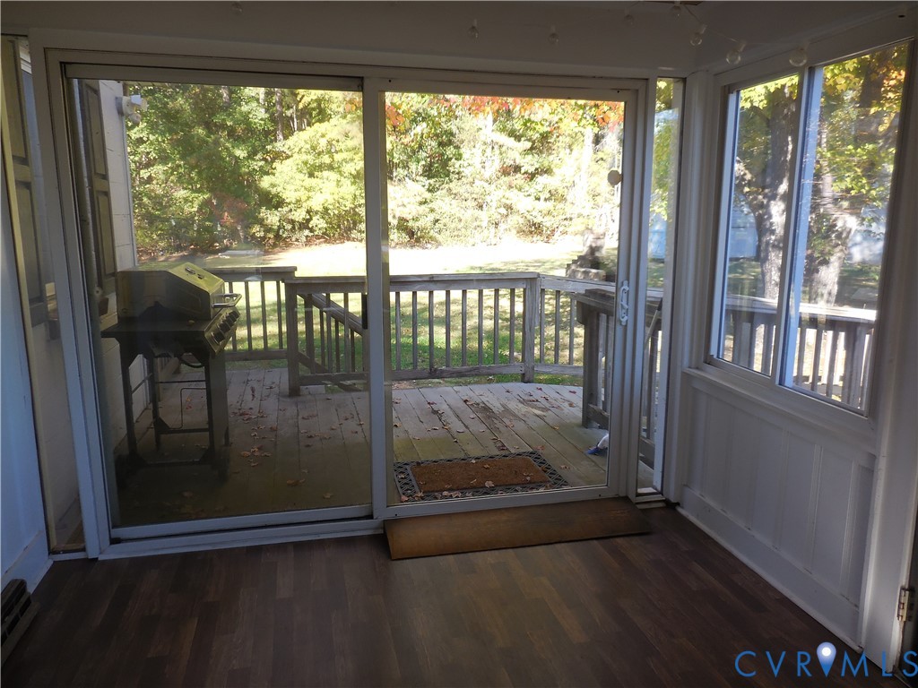 Enclosed sunroom featuring wood-finish flooring, white paneling, expansive sliding glass doors, and an outdoor wood deck