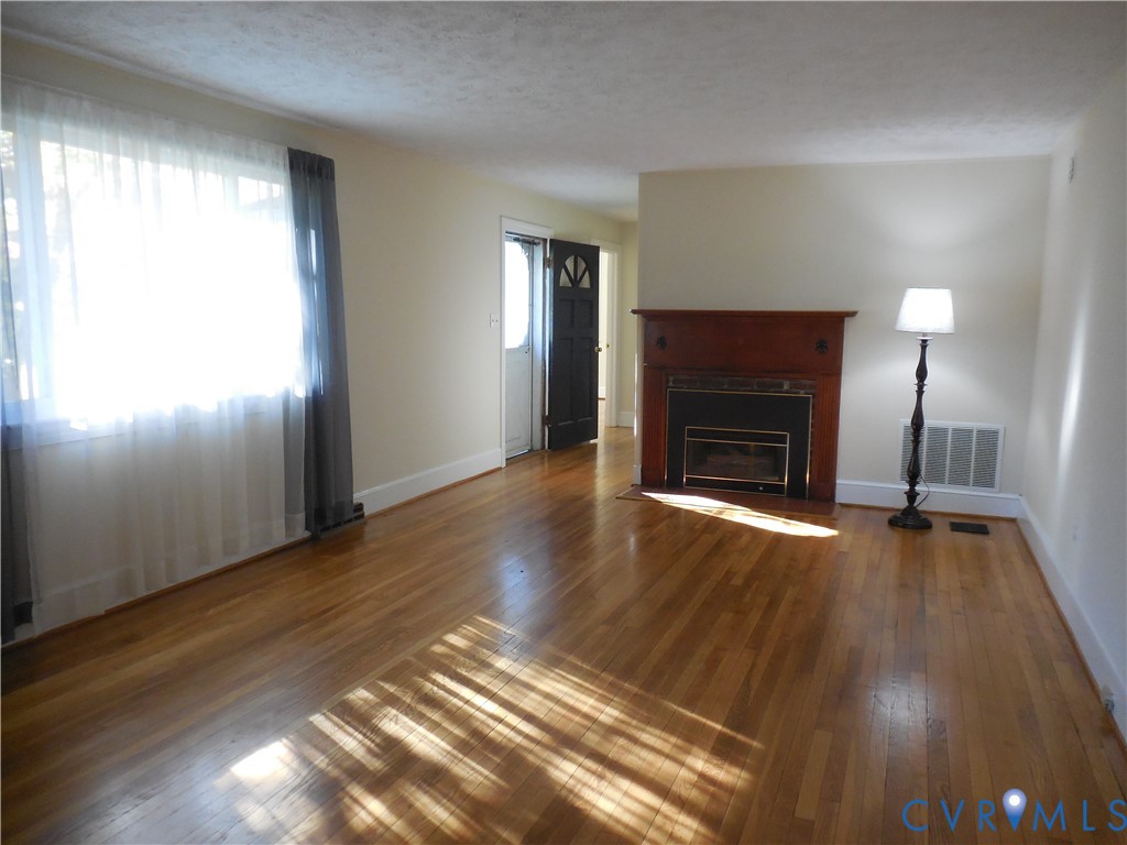 Living area featuring wood-finish flooring, a fireplace with a wood mantel, and large windows