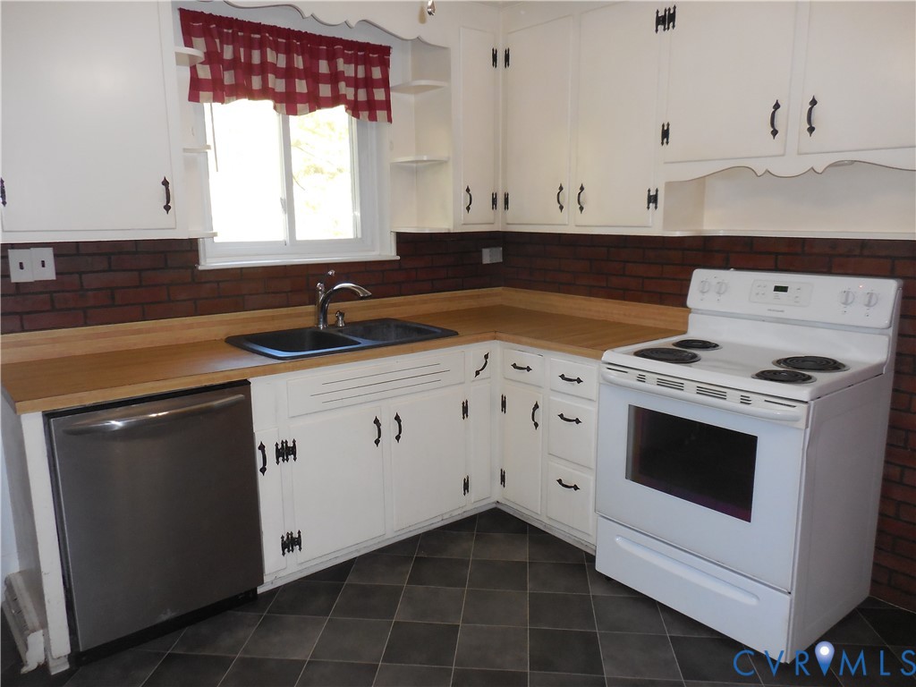 Kitchen featuring white cabinetry, wood-finish countertops, brick backsplash, dual-basin sink, and tile flooring
