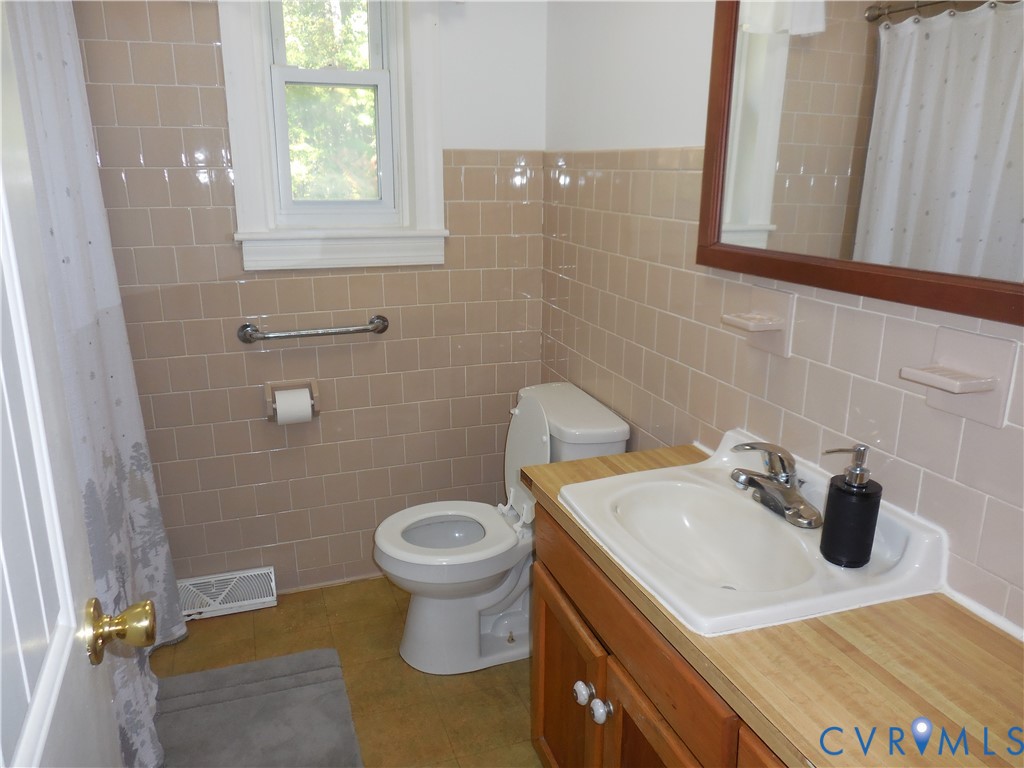 Bathroom featuring tan ceramic wall tile, wood-finish cabinetry, inset sink with metal hardware, and a framed mirror