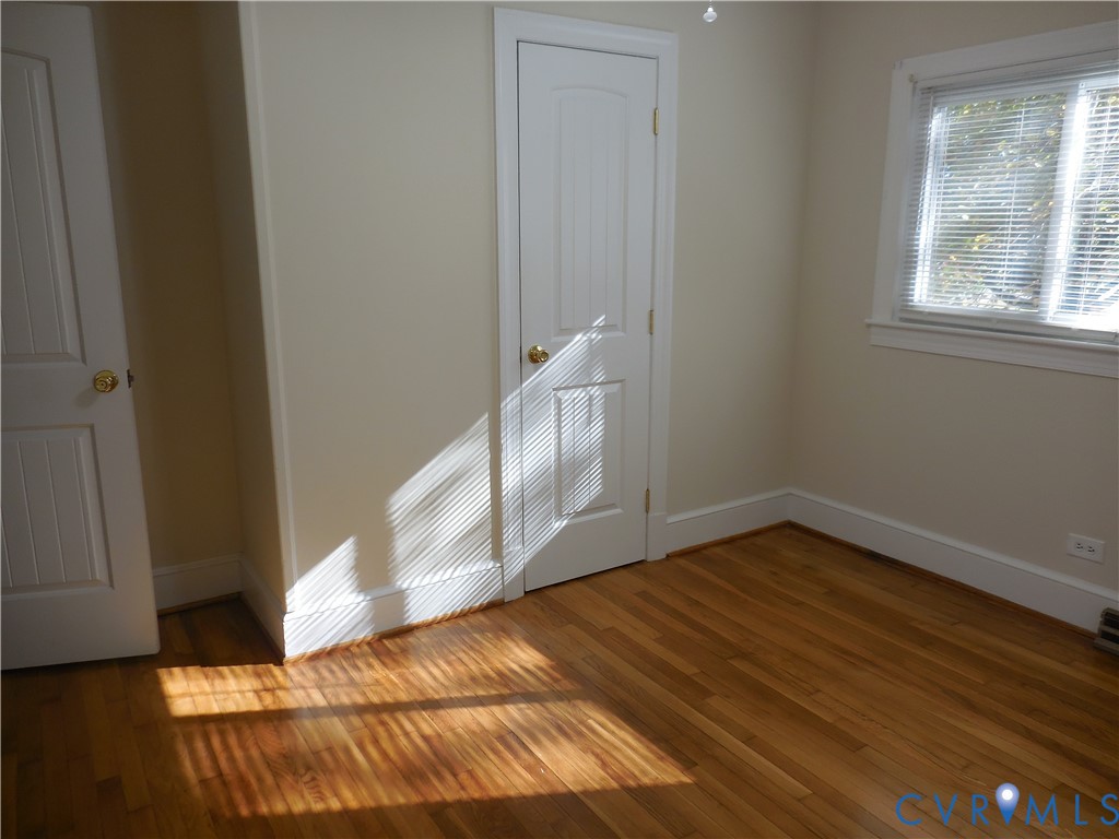 Room featuring wood-finish flooring, two-panel interior doors with brass-tone hardware, and window with white casing