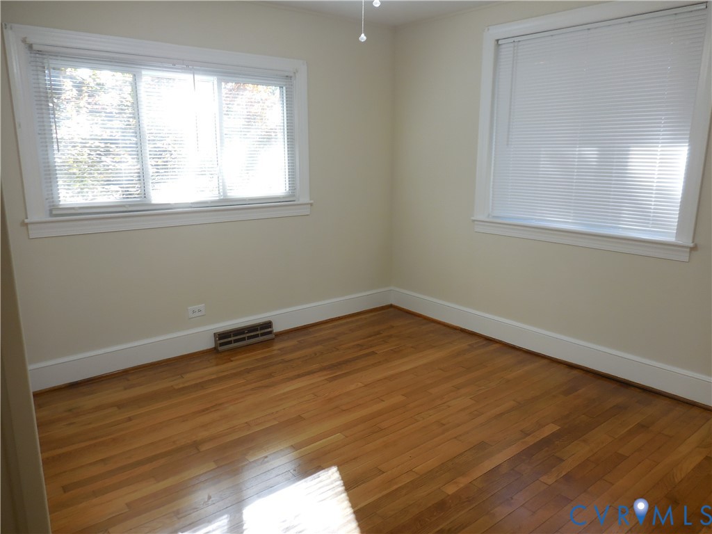 Wood-finish flooring, neutral wall tones, and dual windows with horizontal blinds