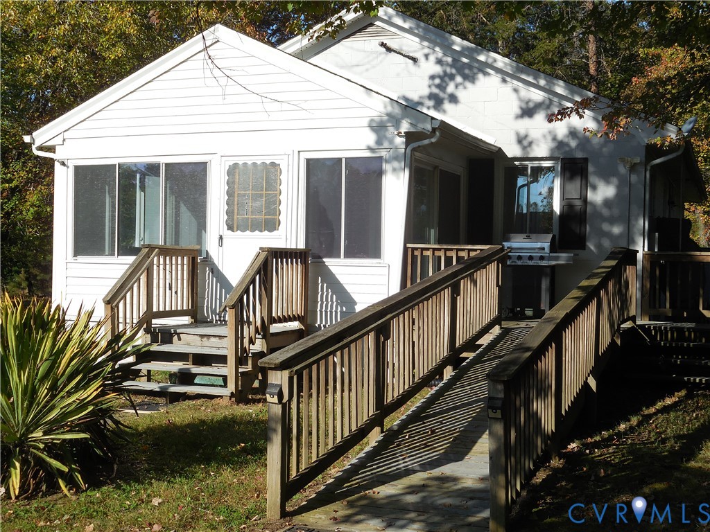 White siding exterior featuring an enclosed sunroom, wooden deck, and wooden ramp with railings