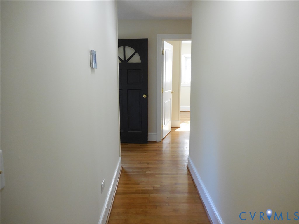 Hallway featuring wood-finish flooring, a dark-toned door with a semi-circle window inlay, and white painted interior doors with traditional millwork