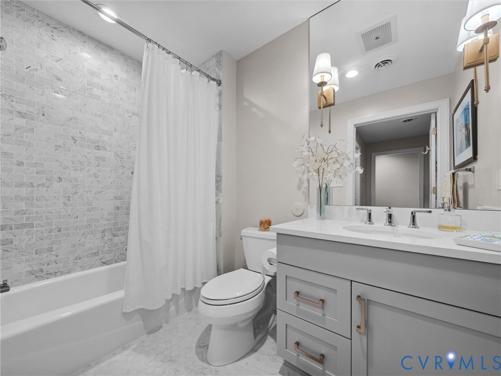 Hall bath with tub/shower with marble tile surround and single vanity.