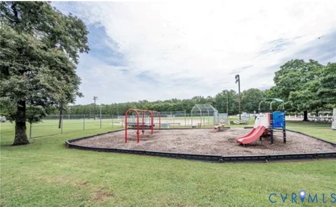 Recreational area featuring a playground with slides and swings, wood-chip ground cover, manicured lawn, perimeter fencing, and mature trees Recreational area featuring a playground with slides and swings, wood-chip ground cover, manicured lawn, perimeter fencing, and mature trees
