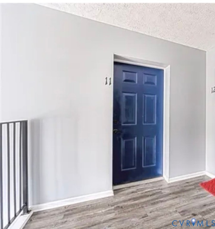 Six-panel navy blue entrance door featuring a metallic handle set, set within light-toned walls and wood-finish flooring with a metal railing Six-panel navy blue entrance door featuring a metallic handle set, set within light-toned walls and wood-finish flooring with a metal railing