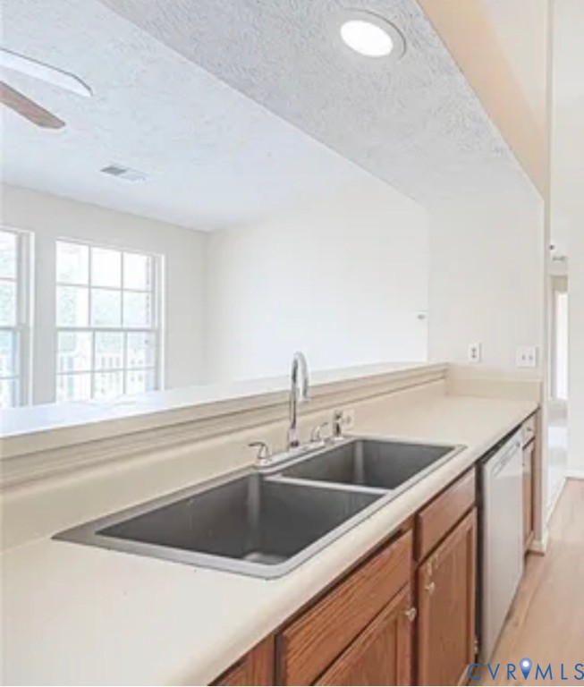 Kitchen workspace featuring a dual-basin stainless steel sink, gooseneck faucet, light-toned solid surface countertops, and wood-finish cabinetry