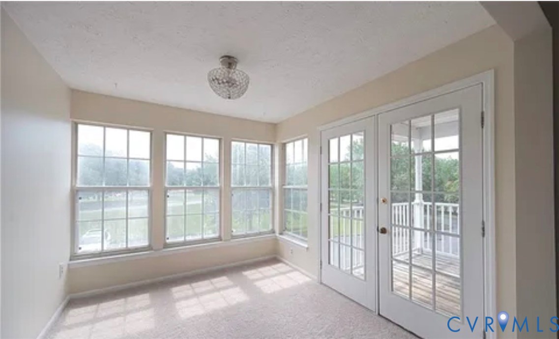 Interior space featuring multi-pane windows, double glass-panel doors with exterior access, neutral carpeting, and a polished metal globe-style ceiling fixture Interior space featuring multi-pane windows, double glass-panel doors with exterior access, neutral carpeting, and a polished metal globe-style ceiling fixture