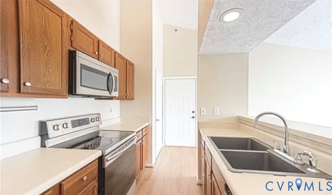 Kitchen featuring wooden cabinetry, stainless steel microwave and oven, high ceilings, wood-finish flooring, and a double-basin sink