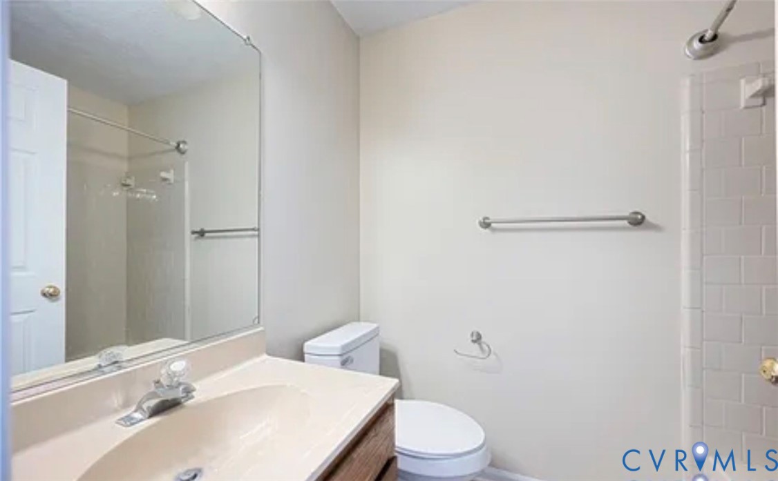 Bathroom featuring a vanity with integrated sink, large wall-mounted mirror, ceramic tile shower surround, and brushed nickel hardware