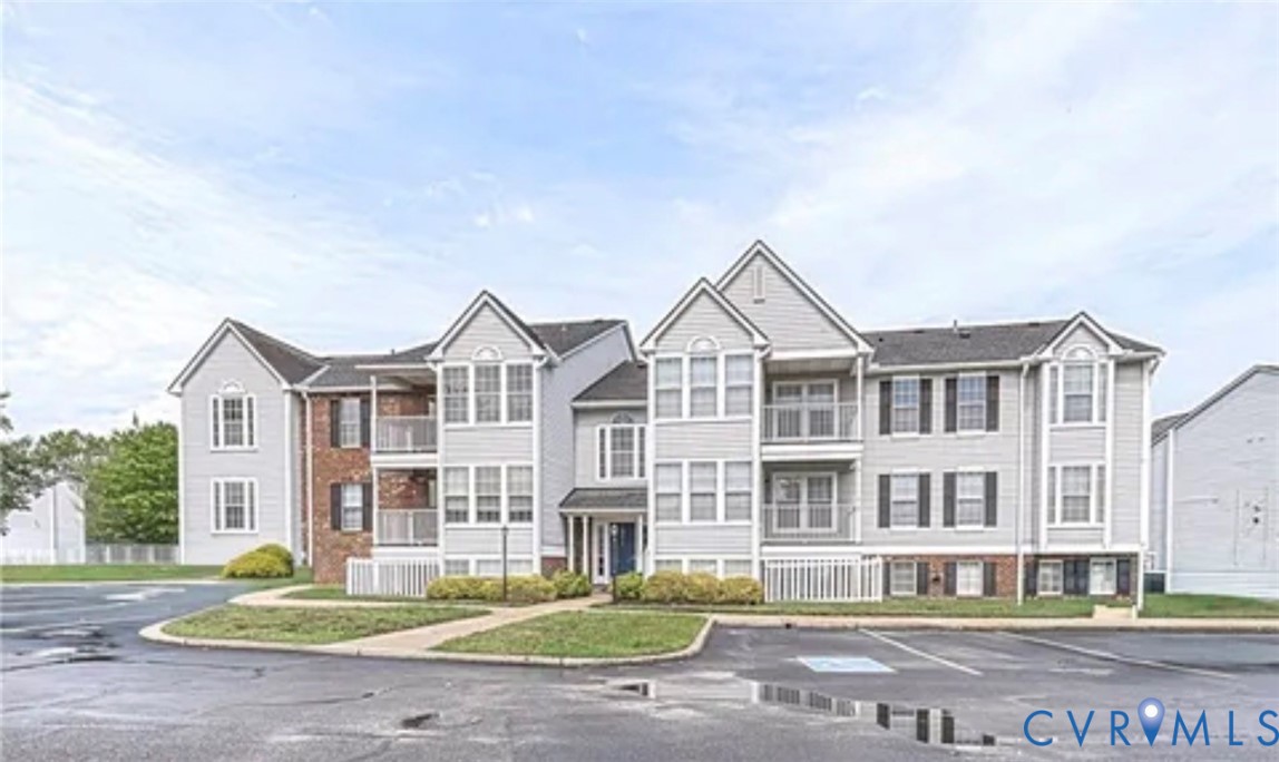 Multi-level building exterior featuring gray siding, brick veneer accents, multiple balconies with metal railings, and a shingled roof Multi-level building exterior featuring gray siding, brick veneer accents, multiple balconies with metal railings, and a shingled roof