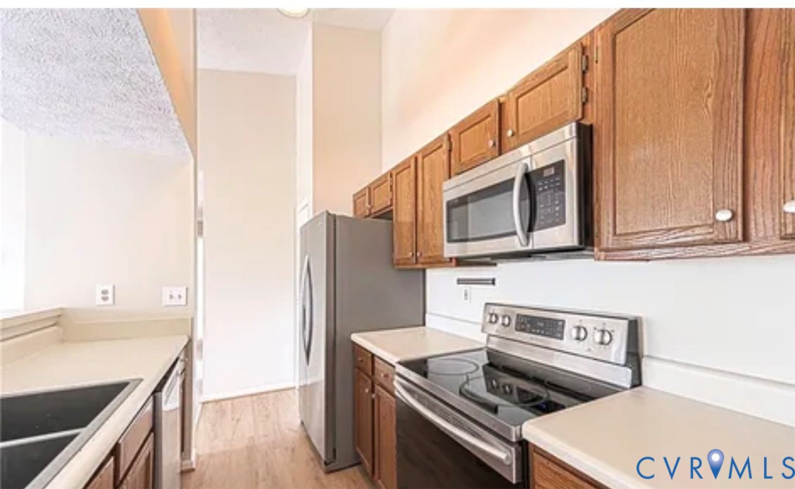 Kitchen featuring wood cabinetry, stainless steel appliances, neutral countertops, and wood-finish flooring