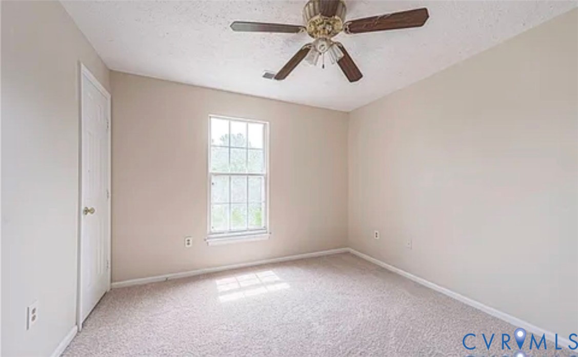 Neutral-toned interior room featuring wall-to-wall carpeting, a multi-pane window, and a ceiling fan with integrated lighting