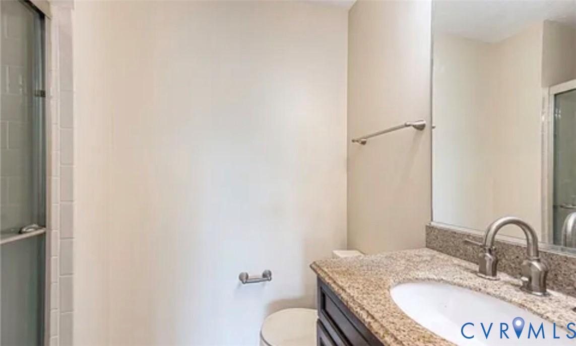 Bathroom featuring a stone-surface vanity with an integrated basin, brushed metal faucet, large wall-mounted mirror, and glass-enclosed shower