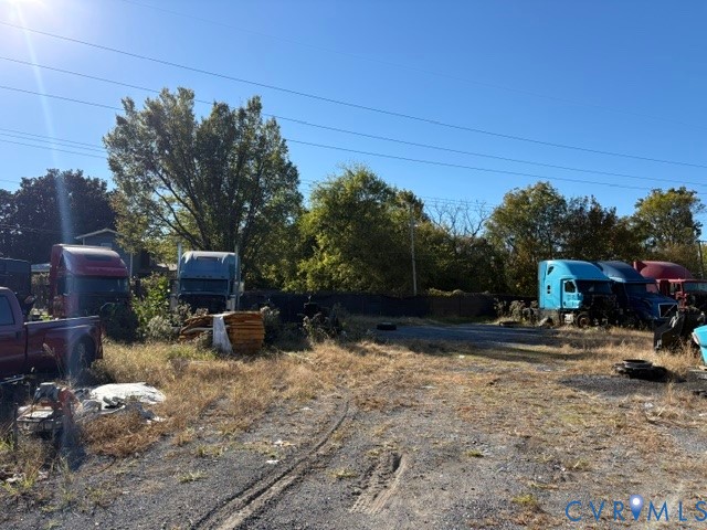 Expansive exterior lot featuring a stabilized gravel surface, mature tree line, and perimeter mesh fencing