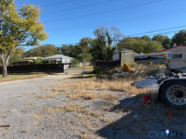 Gravel lot featuring mature trees and a chain-link perimeter fence