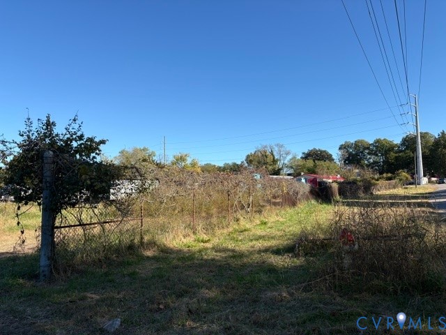 Expansive unimproved lot featuring chain-link fencing, mature trees, and street-level utility access