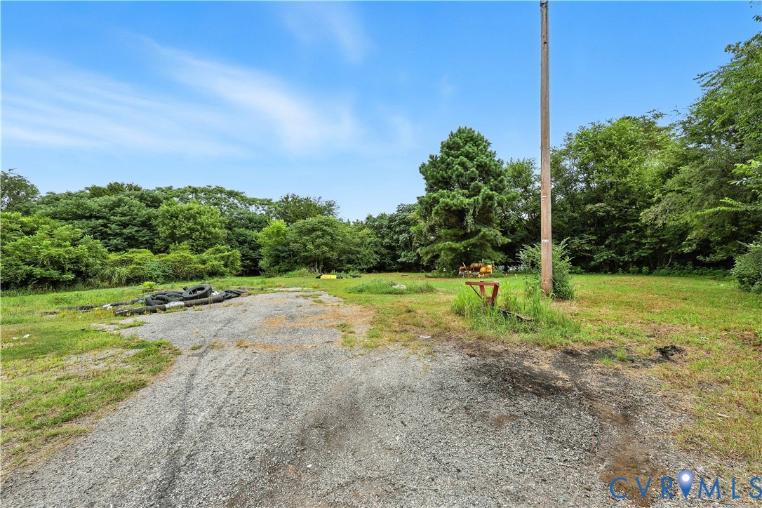 Expansive lot featuring gravel-surfaced drive area, open grassy terrain, and mature perimeter trees