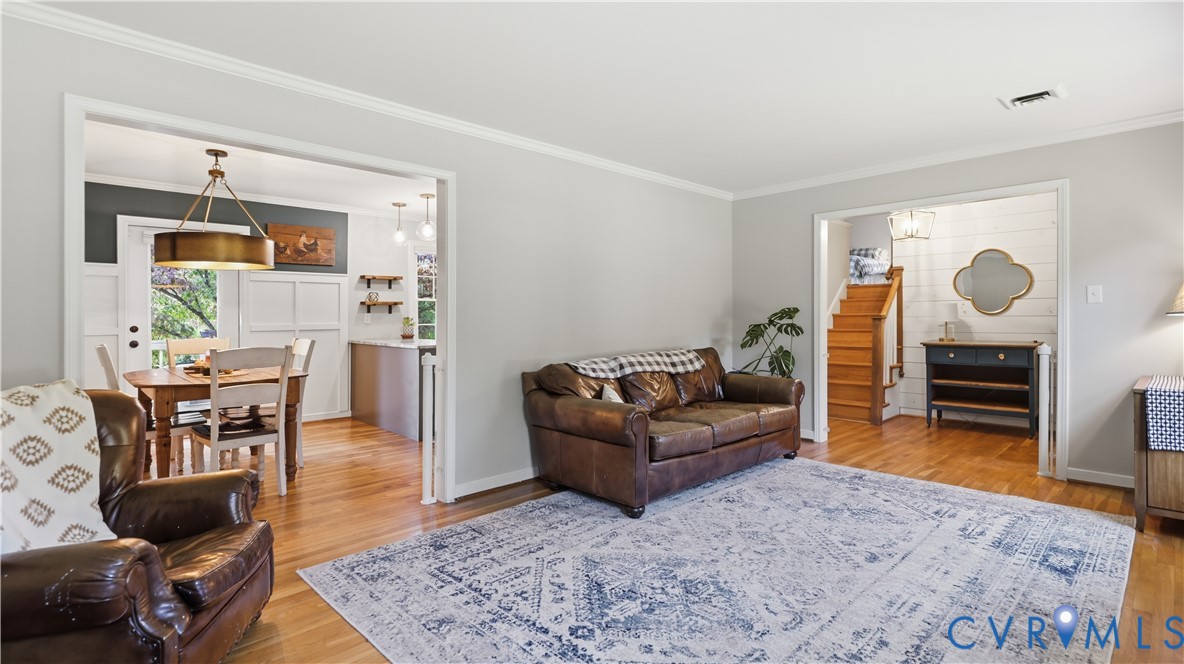 Living space featuring wood-finish flooring, crown molding, and two open-entryways with white trim accents