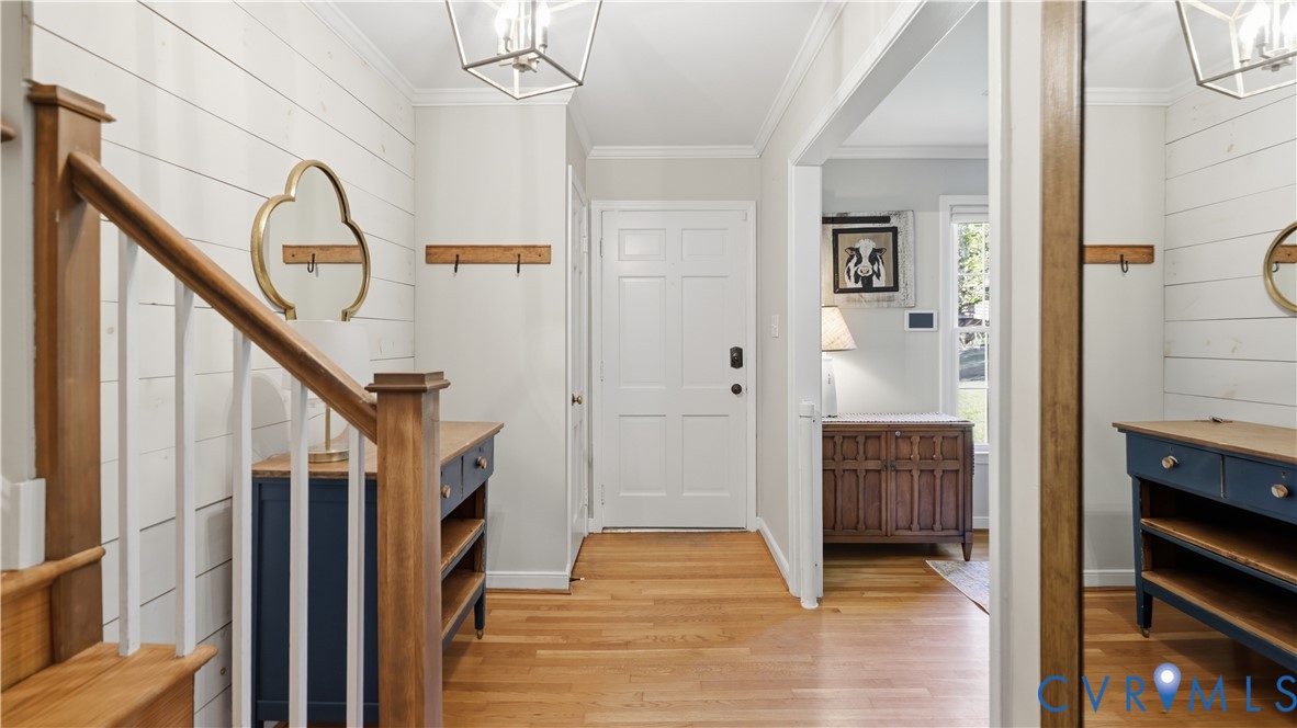 Entryway featuring horizontal plank wall detailing, wood-finish flooring, a wood-accented staircase, and geometric hanging light fixtures