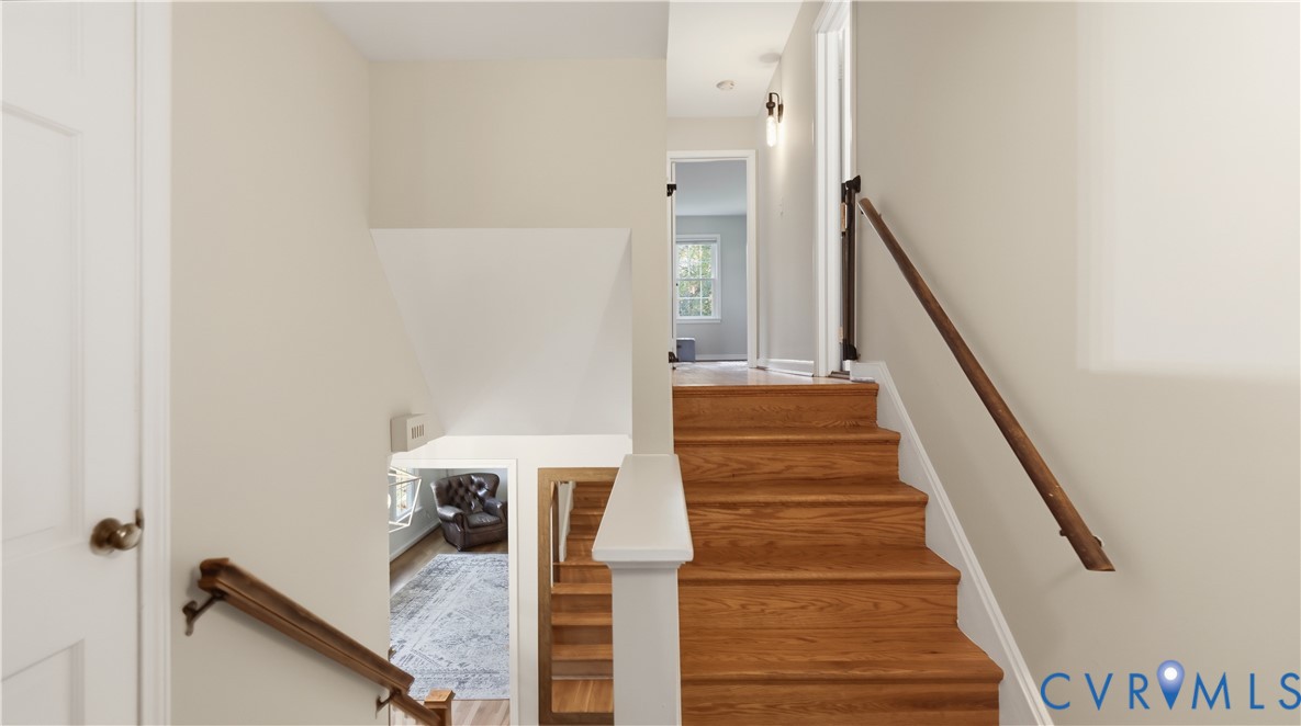 Staircase featuring wood-finish treads and wall-mounted handrails with a white half-wall balustrade