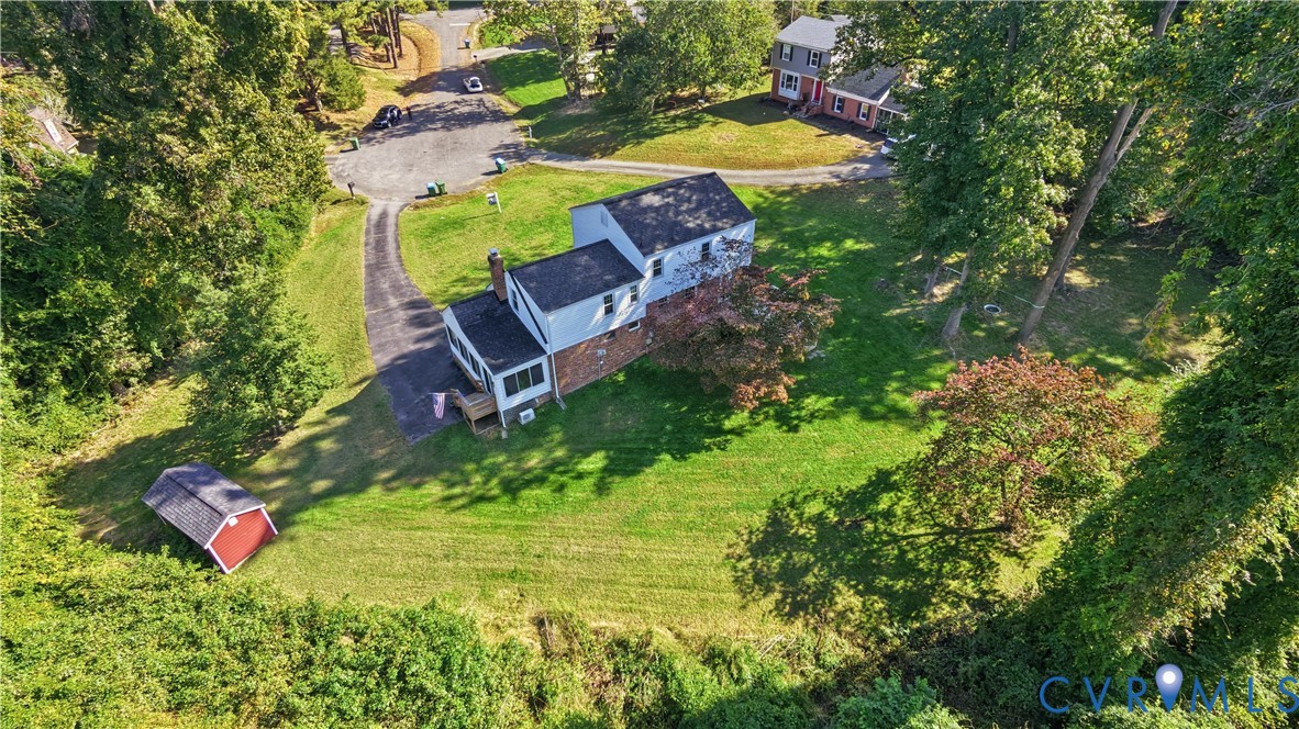 Multi-level residence featuring brick and siding exterior, paved driveway, detached storage structure, and expansive lot with mature trees