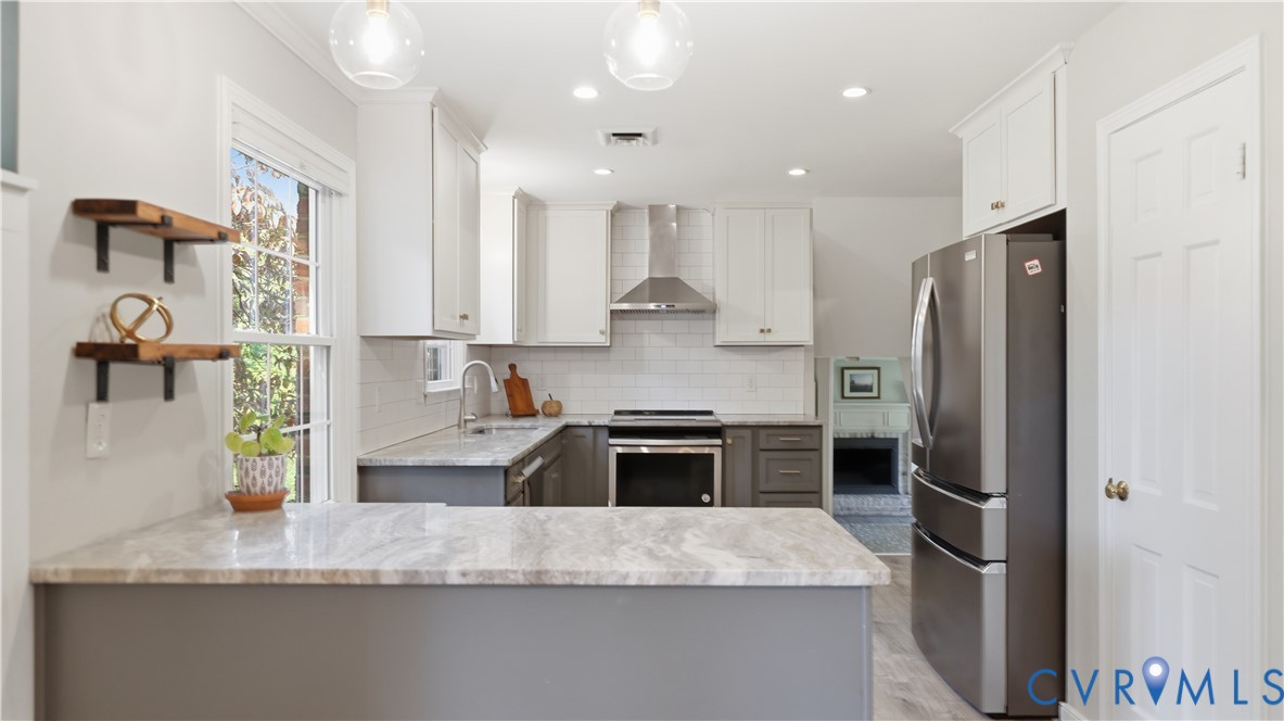 Kitchen featuring light stone-patterned countertops, white shaker-style upper cabinetry, subway tile backsplash, stainless steel appliances, and dual pendant lighting