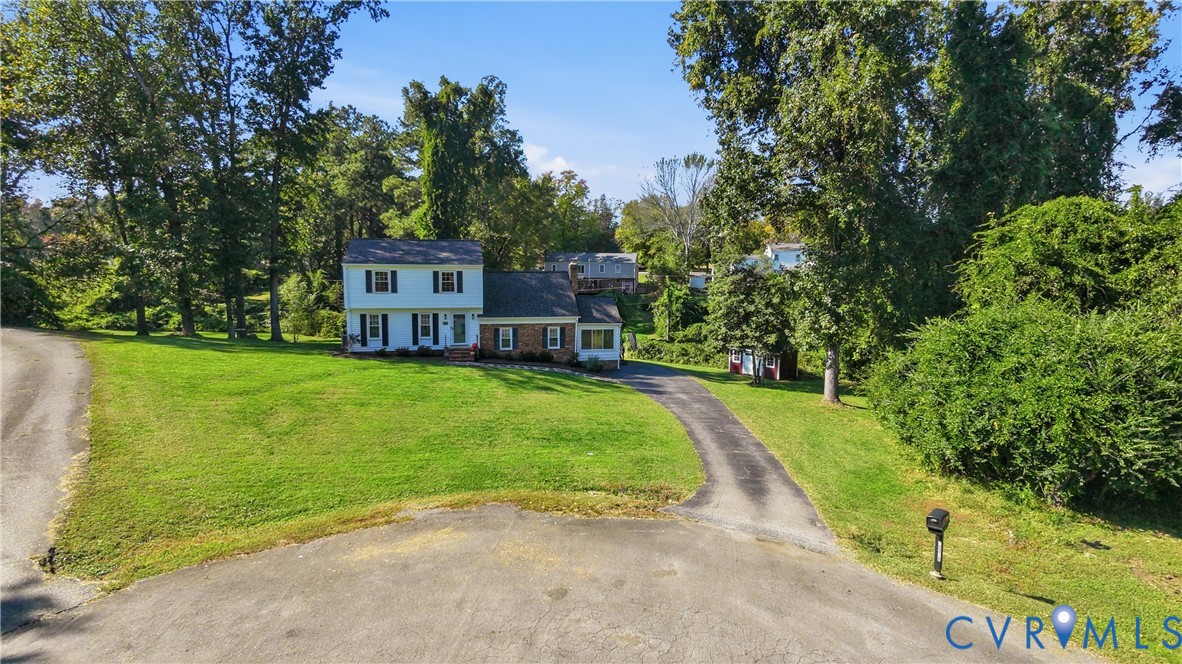 Two-story residence featuring a brick and siding exterior, expansive lawn, mature perimeter trees, and an asphalt driveway