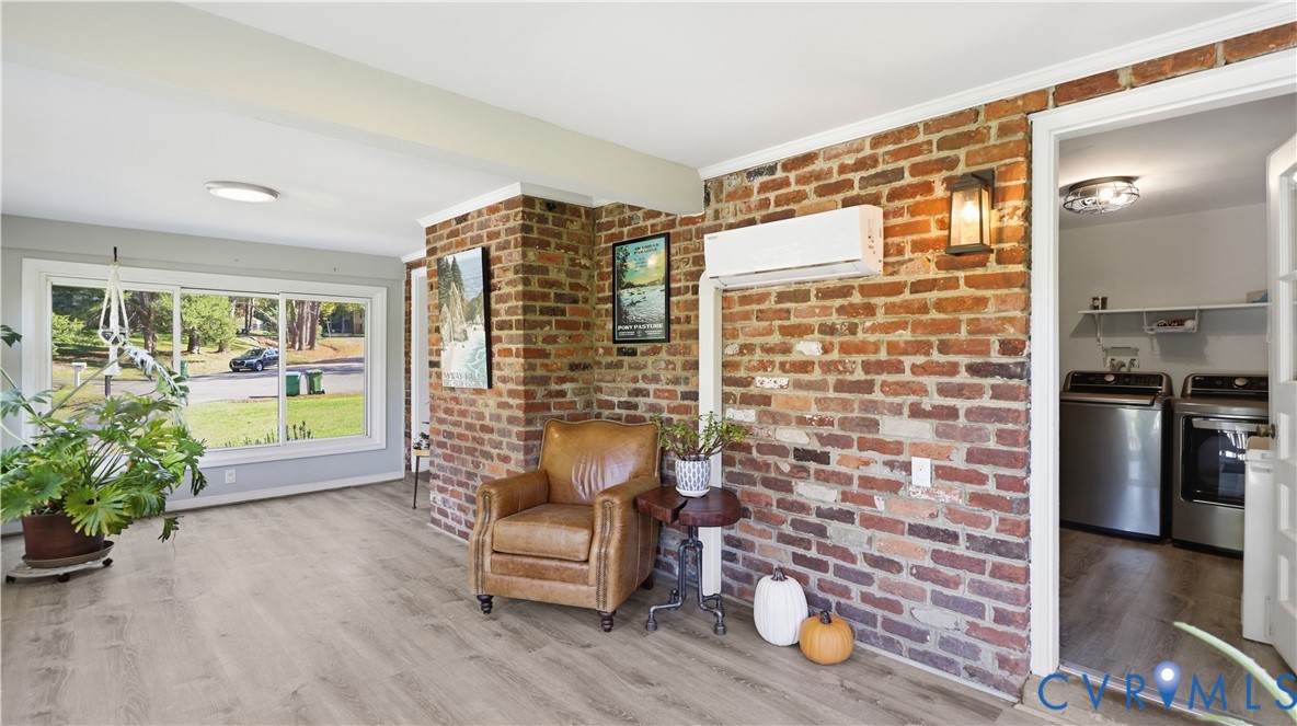 Exposed brick accent wall featuring a wall-mounted ductless climate control unit, large-pane picture window, wood-finish flooring, and recessed ceiling lighting
