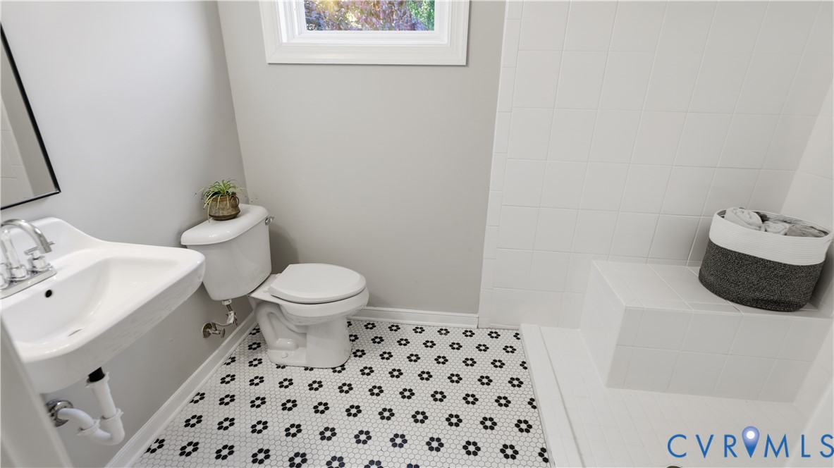 Bathroom featuring a wall-mounted sink with chrome faucet, hexagonal patterned floor tile, white square-tiled shower surround, and built-in shower bench