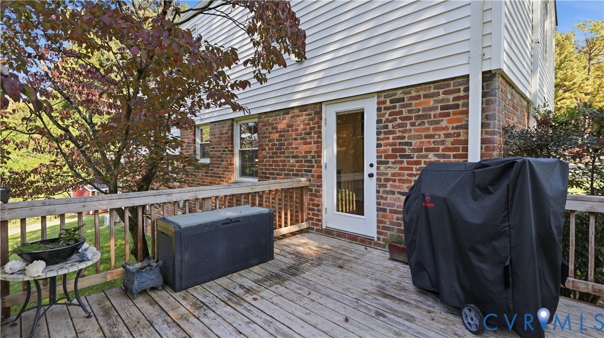 Exterior wood deck with a traditional railing, multi-toned brick masonry, white horizontal siding, and a glass-paneled entry door