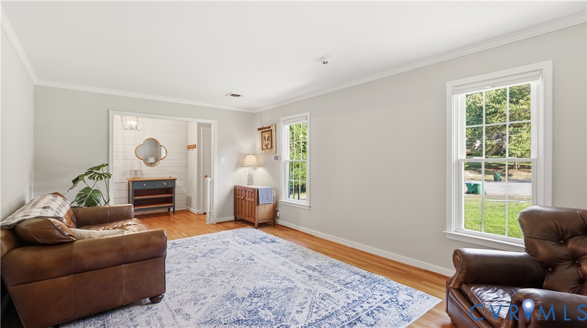 Living area featuring wood-finish flooring, crown molding, multi-pane windows, and white-paneled accent wall detail