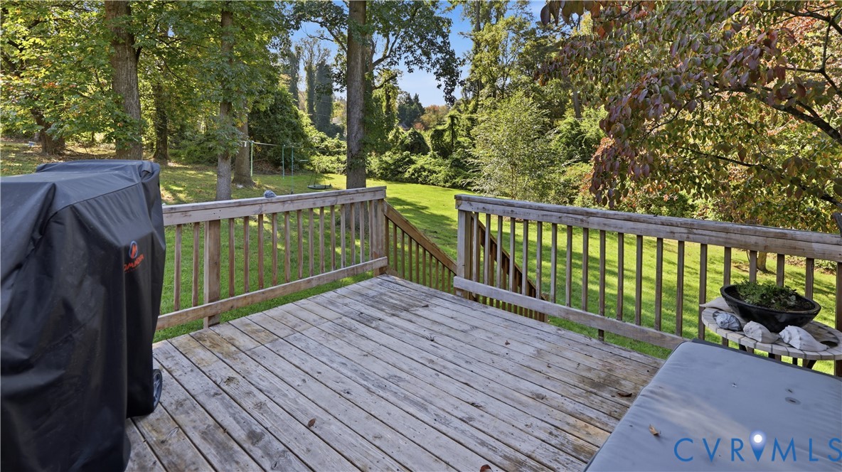 Elevated wood deck with baluster railing, overlooking a expansive grass lawn bordered by mature trees