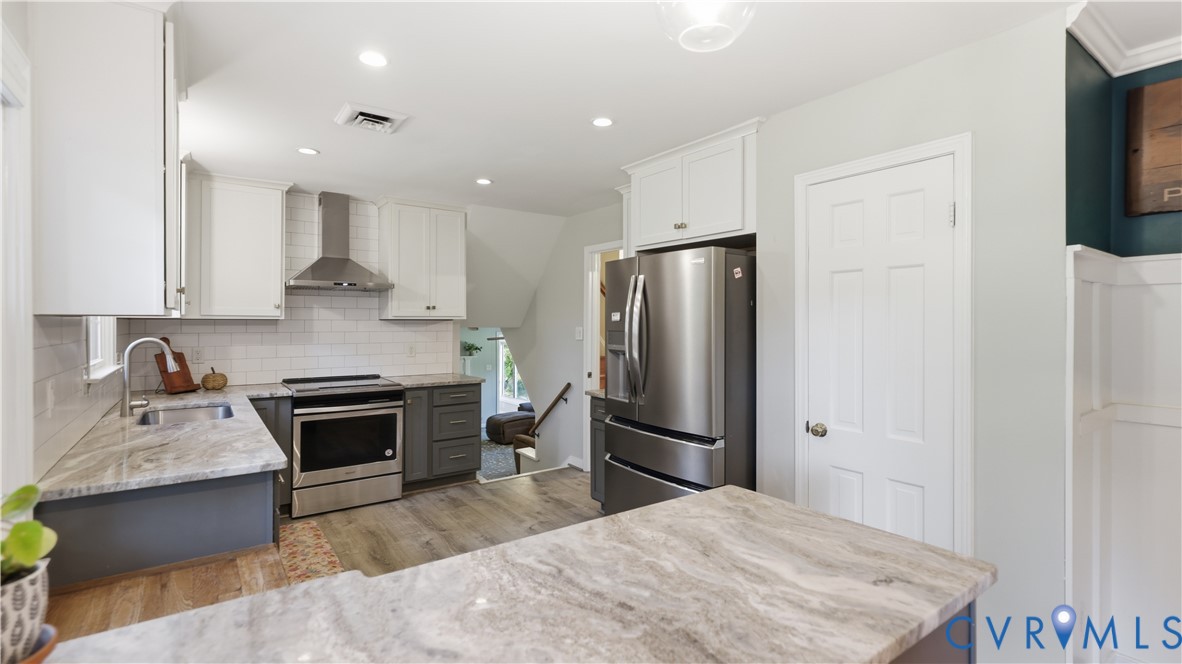 Kitchen featuring stone-finish countertops, stainless steel appliances, shaker-style cabinetry, a white subway tile backsplash, and wood-finish flooring