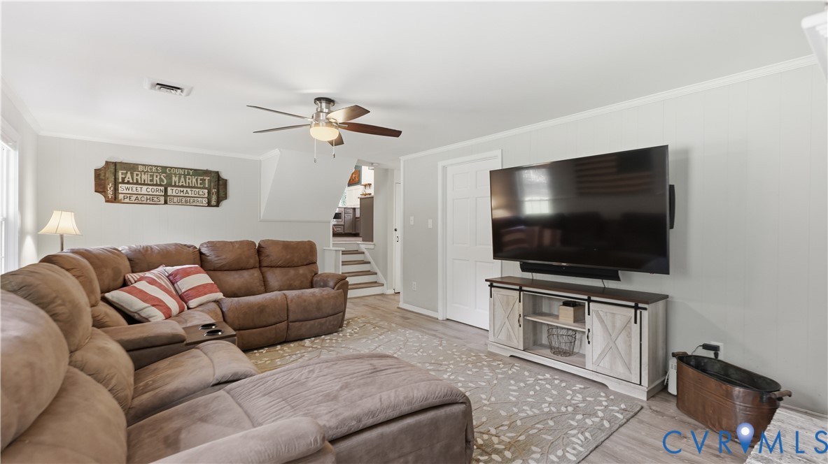 Living area featuring light-toned wood-finish flooring, a ceiling fan with integrated lighting, and a six-panel interior door