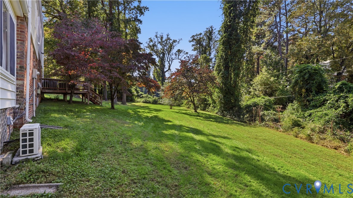 Expansive backyard featuring a tiered wooden deck, brick and siding exterior, mature hardwood trees, and sloped lawn