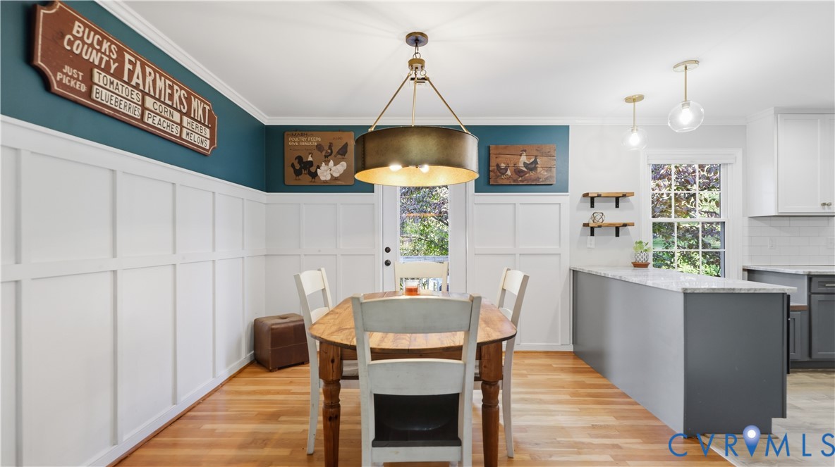 Board and batten wainscoting, wood-finish flooring, drum-style chandelier, and granite-topped kitchen peninsula