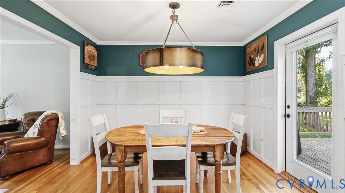 Dining space featuring white wainscoting, wood-finish flooring, a drum pendant light fixture, and a glass-paneled exterior door