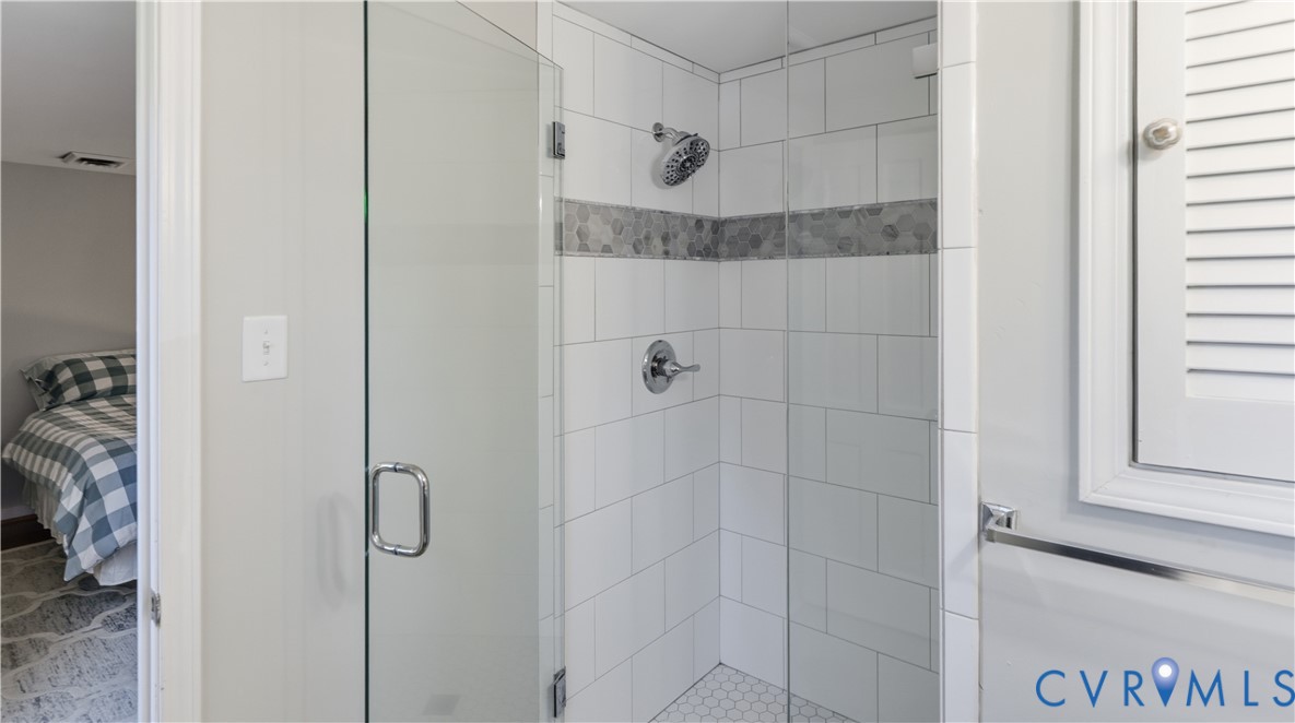Walk-in shower featuring a frameless glass door, white subway tile surround with a decorative mosaic inlay, chrome fixtures, and white hexagonal tile flooring