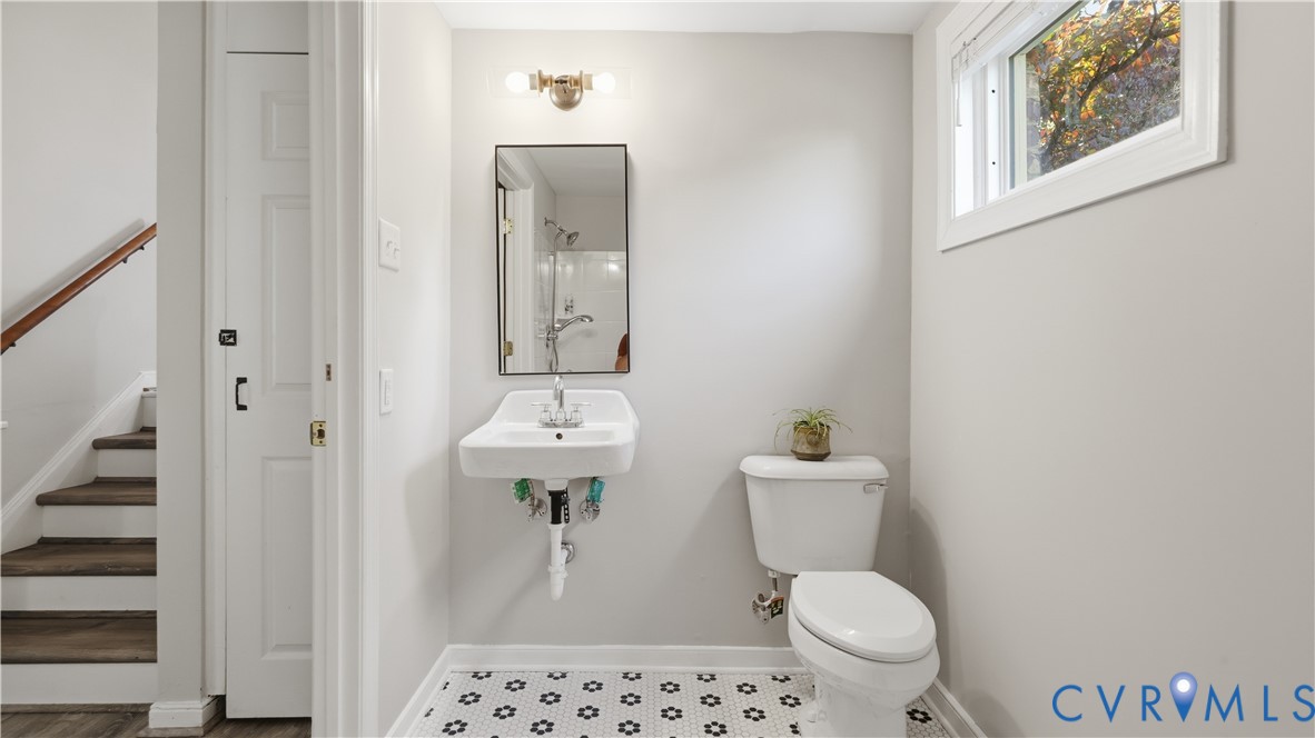 Wall-mounted porcelain sink with chrome fixtures, rectangular mirror with metal frame, and geometric patterned floor tile