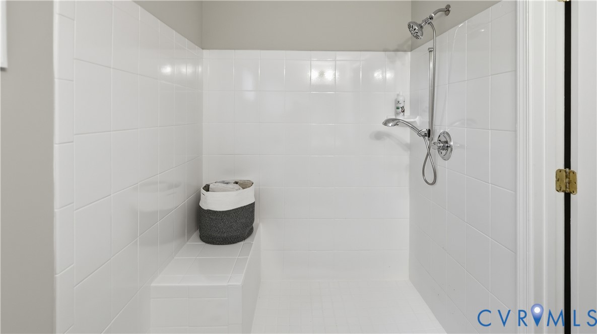 Walk-in shower enclosure featuring white wall tiling, integrated tile bench, and chrome hardware including a detachable showerhead