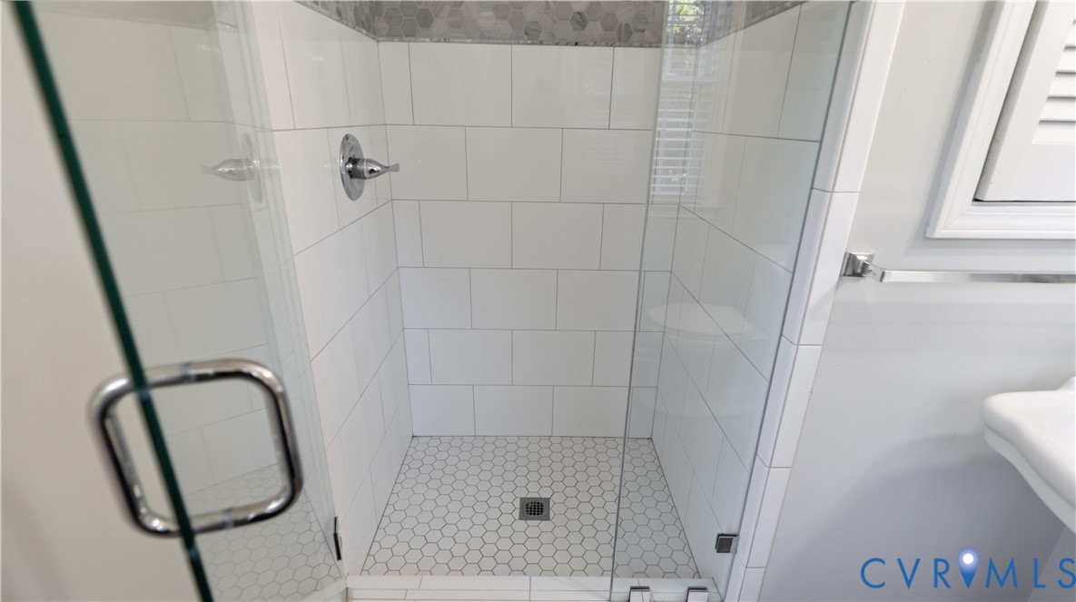 Walk-in shower featuring white subway wall tile, hexagonal floor tile, chrome fixtures, and a frameless glass door
