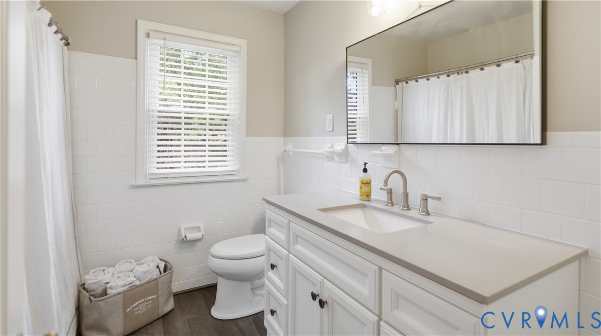 Bathroom featuring a white shaker-style vanity with a solid surface countertop, undermount sink, framed wall mirror, and subway tile wainscoting