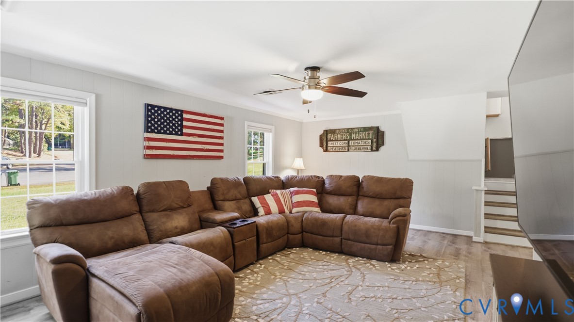 Living area featuring wood-finish flooring, ceiling fan with light fixture, and multiple windows