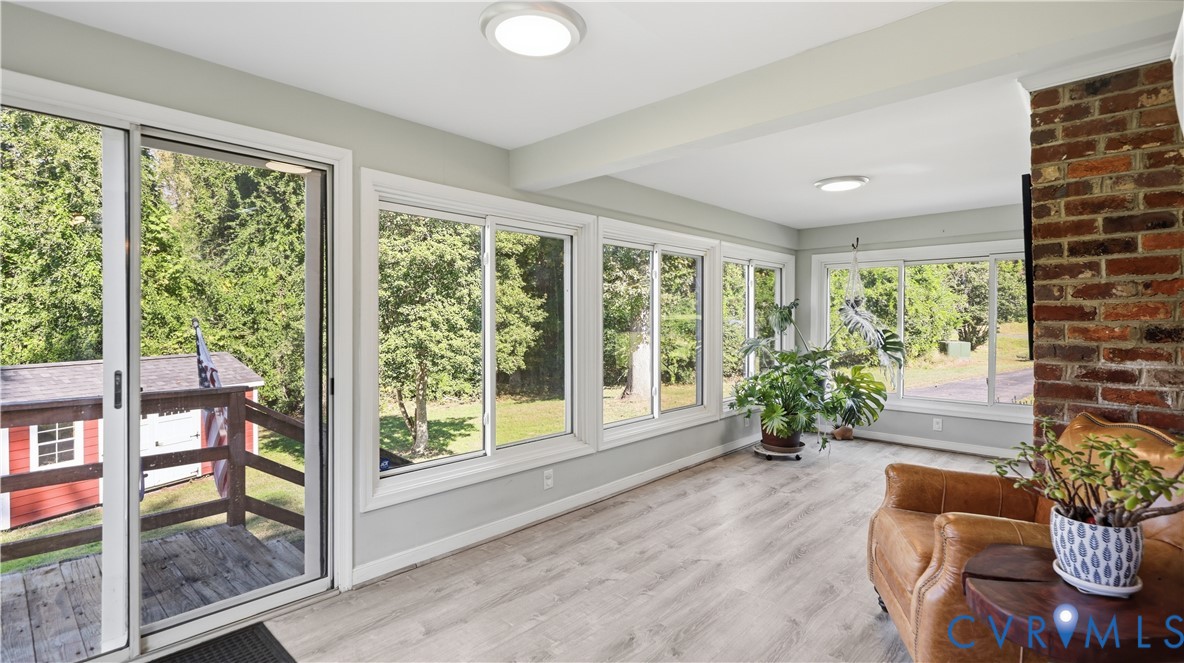 Sunroom featuring light-toned wood-finish flooring, multiple expansive windows, a floor-to-ceiling brick chimney breast, and a sliding glass door providing access to a deck