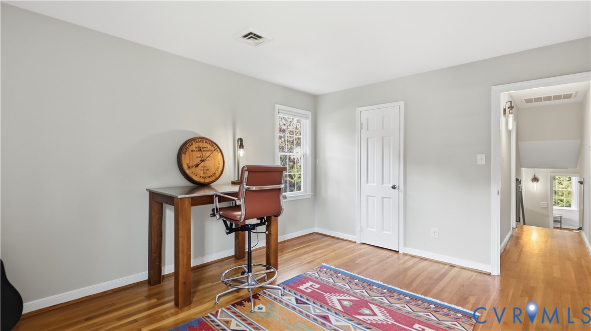 Room featuring light-toned neutral walls, wood-finish flooring, a single-panel interior door, and a multi-pane window